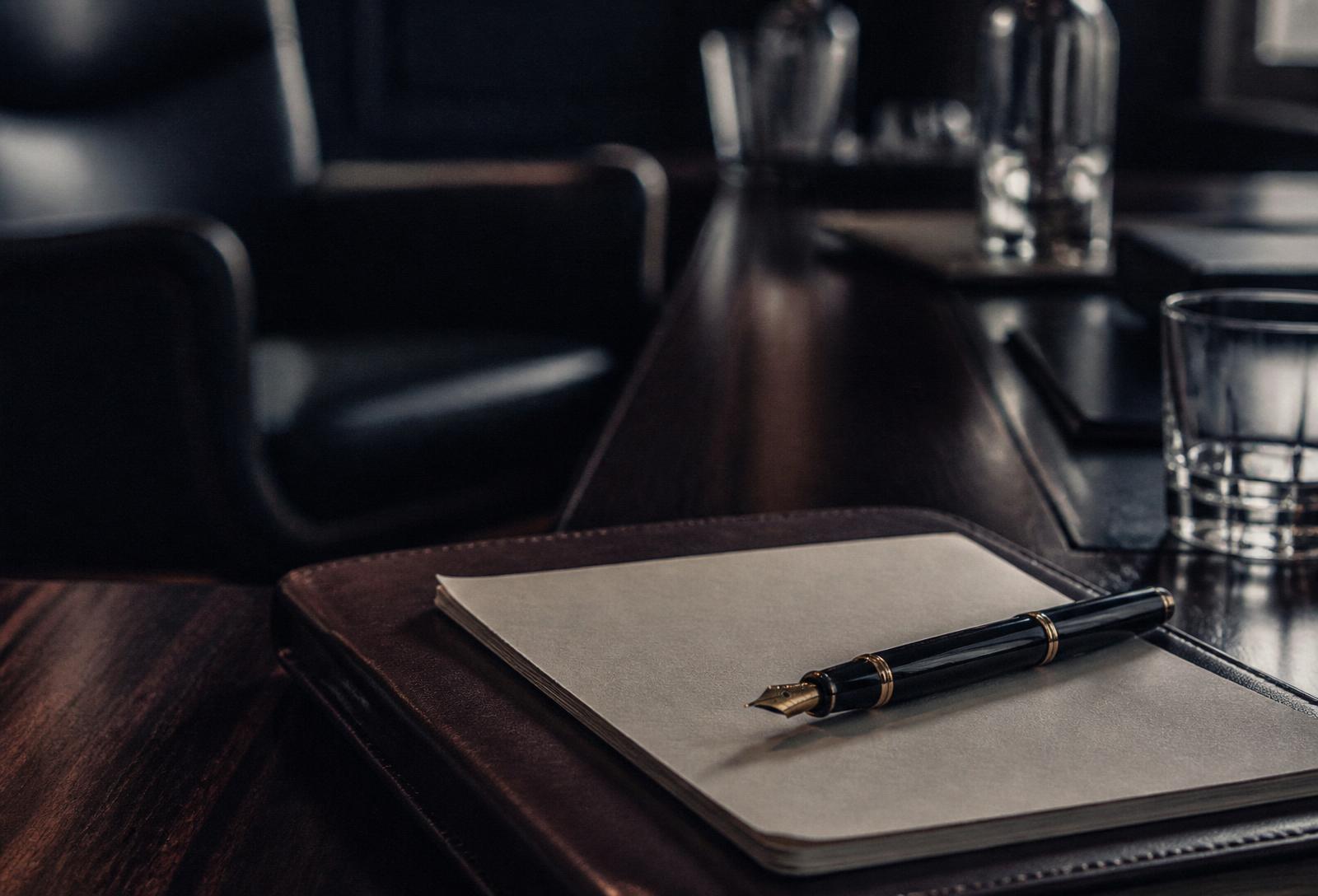 Leather-bound notebook and fountain pen resting on a dark walnut boardroom table, softly lit